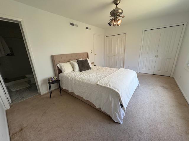 carpeted bedroom featuring connected bathroom, visible vents, multiple closets, and baseboards
