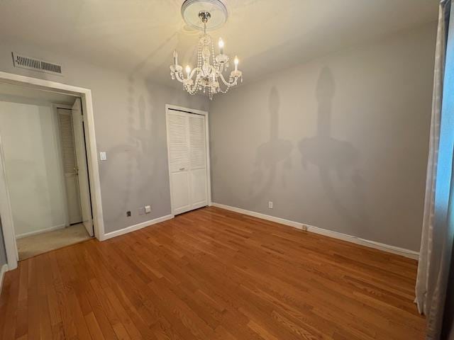 unfurnished bedroom with wood finished floors, visible vents, a chandelier, and baseboards