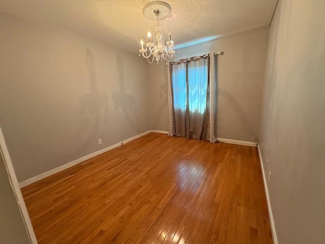 spare room featuring hardwood / wood-style floors, a notable chandelier, and baseboards