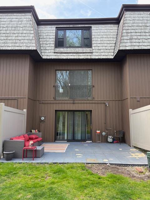 rear view of house featuring mansard roof, fence, and a patio area