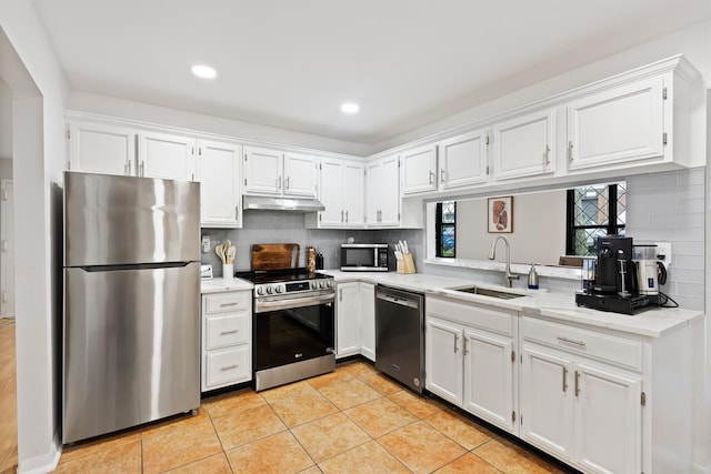 kitchen with white cabinetry, under cabinet range hood, a sink, appliances with stainless steel finishes, and backsplash