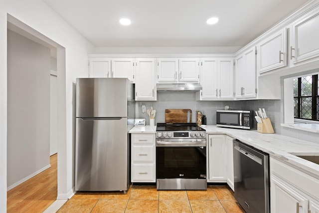 kitchen featuring light stone countertops, white cabinetry, under cabinet range hood, backsplash, and stainless steel appliances