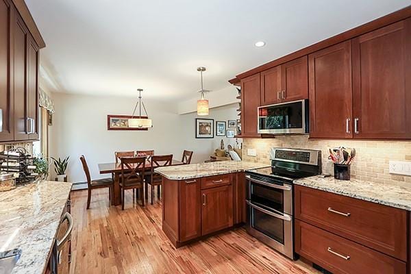 kitchen with light wood-style floors, a peninsula, appliances with stainless steel finishes, and tasteful backsplash