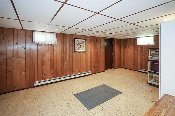 below grade area with tile patterned floors, a baseboard heating unit, wood walls, and a paneled ceiling