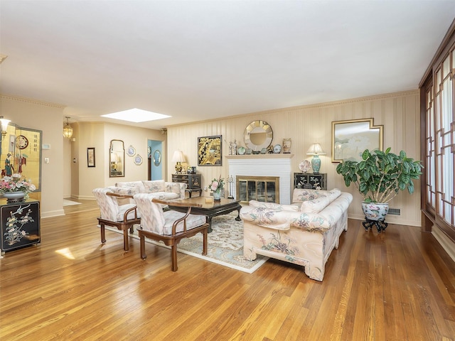living area with crown molding, a brick fireplace, wood finished floors, and a skylight