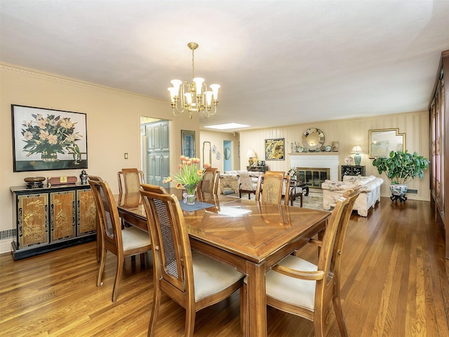 dining area featuring ornamental molding, an inviting chandelier, a glass covered fireplace, and wood finished floors