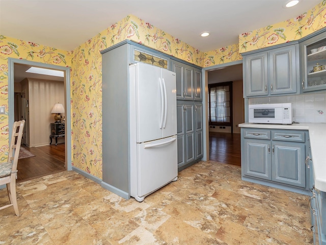 kitchen with gray cabinets, light countertops, baseboards, wallpapered walls, and white appliances