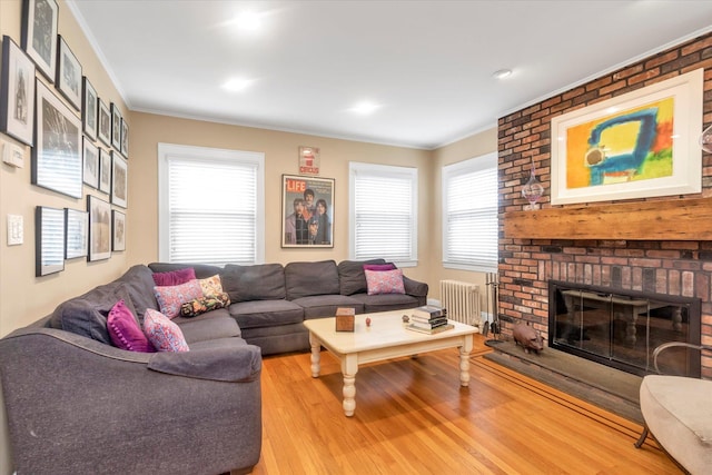 living room with radiator heating unit, wood finished floors, crown molding, and a brick fireplace