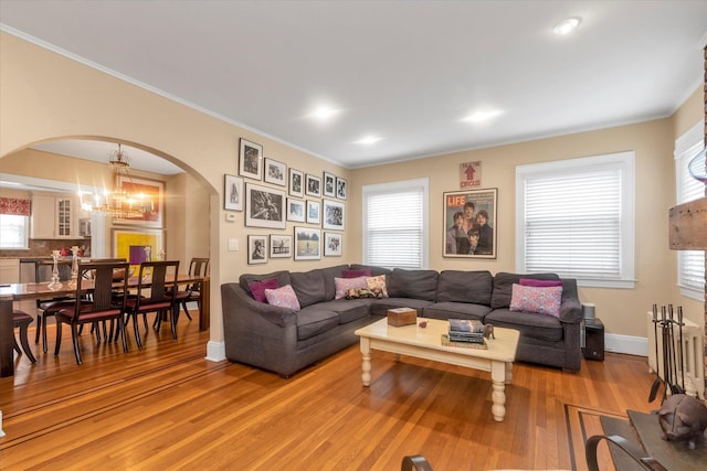 living room featuring arched walkways, light wood finished floors, a chandelier, crown molding, and baseboards