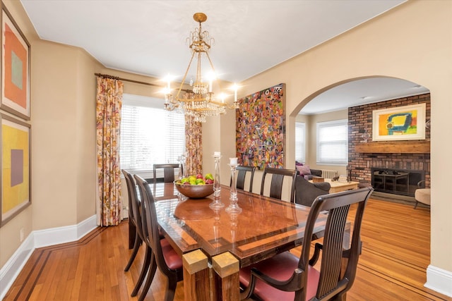 dining room with a chandelier, light wood finished floors, arched walkways, baseboards, and healthy amount of natural light
