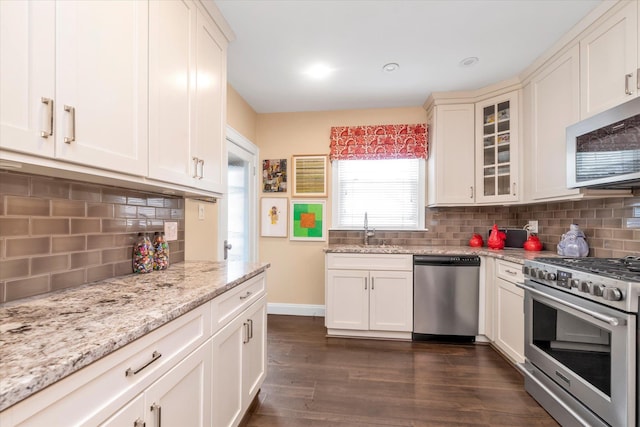 kitchen with appliances with stainless steel finishes, dark wood finished floors, tasteful backsplash, and glass insert cabinets