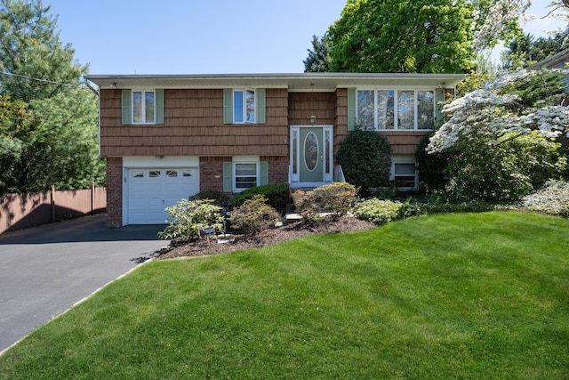 bi-level home featuring a garage, fence, a front yard, brick siding, and driveway