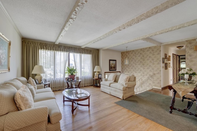 living room with light wood finished floors, a textured ceiling, wallpapered walls, baseboards, and beamed ceiling