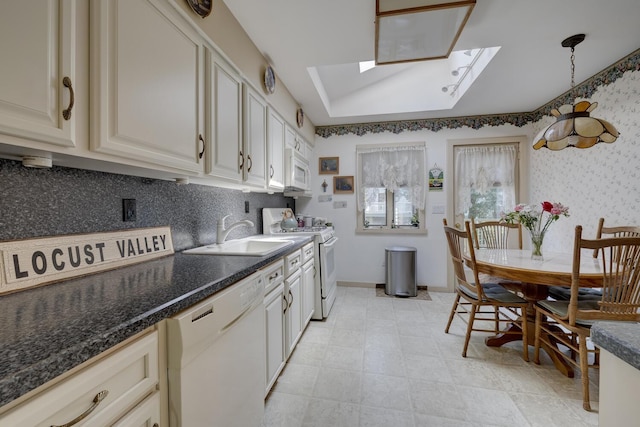 kitchen featuring white appliances, baseboards, tasteful backsplash, a sink, and a skylight