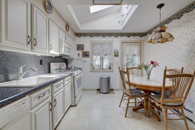 kitchen with dark countertops, white appliances, white cabinets, a sink, and a skylight