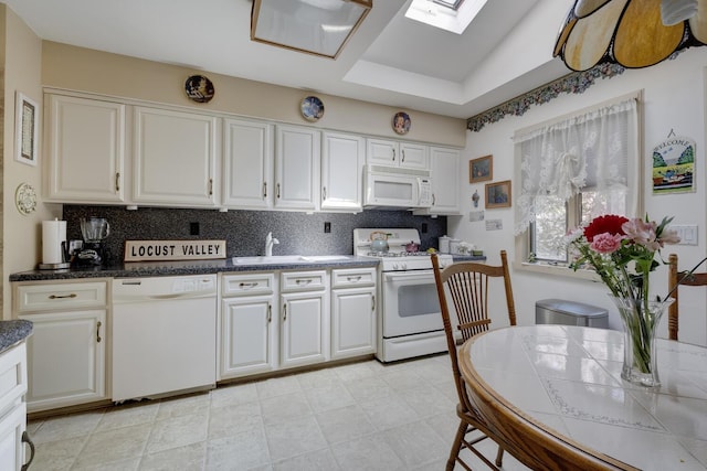 kitchen featuring a skylight, white cabinets, backsplash, and white appliances