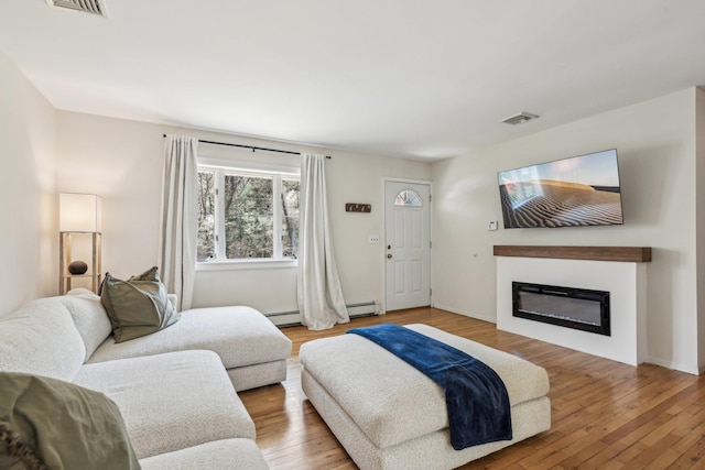 living area with visible vents, wood finished floors, a baseboard radiator, and a glass covered fireplace
