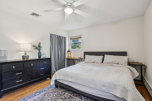 bedroom with a baseboard heating unit, a ceiling fan, visible vents, and wood finished floors