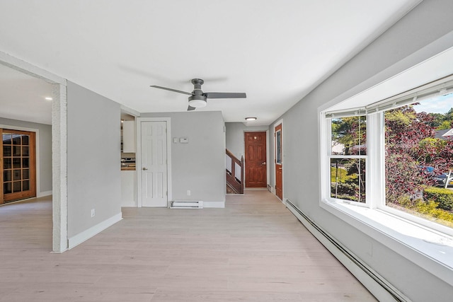 empty room with a baseboard heating unit, light wood-type flooring, ceiling fan, and baseboards