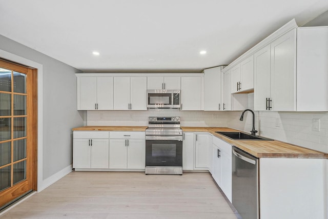 kitchen featuring stainless steel appliances, wood counters, a sink, tasteful backsplash, and recessed lighting