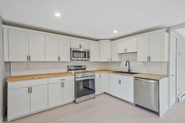 kitchen with appliances with stainless steel finishes, butcher block countertops, a sink, decorative backsplash, and recessed lighting