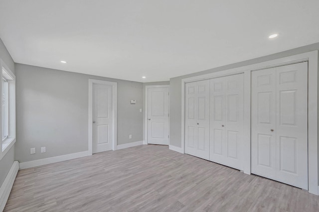 unfurnished bedroom featuring a baseboard heating unit, light wood-style floors, baseboards, recessed lighting, and multiple closets