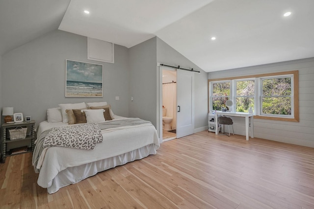 bedroom featuring a barn door, lofted ceiling, light wood-style flooring, recessed lighting, and connected bathroom