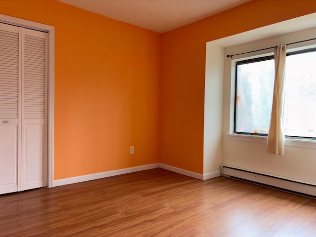 unfurnished bedroom featuring baseboards, a baseboard radiator, light wood-style flooring, and a closet