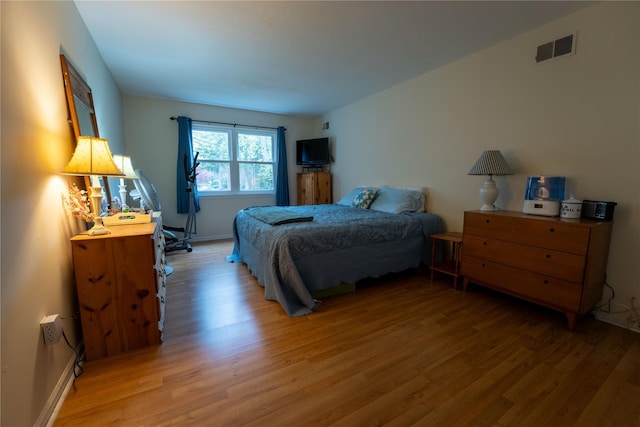 bedroom featuring baseboards, light wood-type flooring, and visible vents