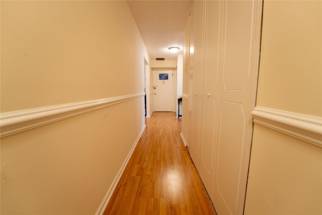 hallway with light wood-style floors, baseboards, and visible vents