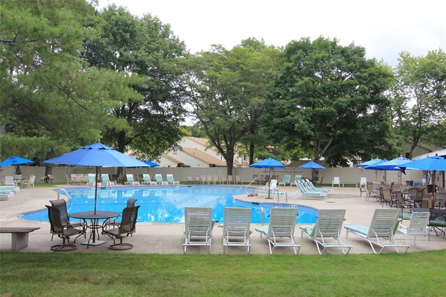 pool with a patio, a lawn, and fence