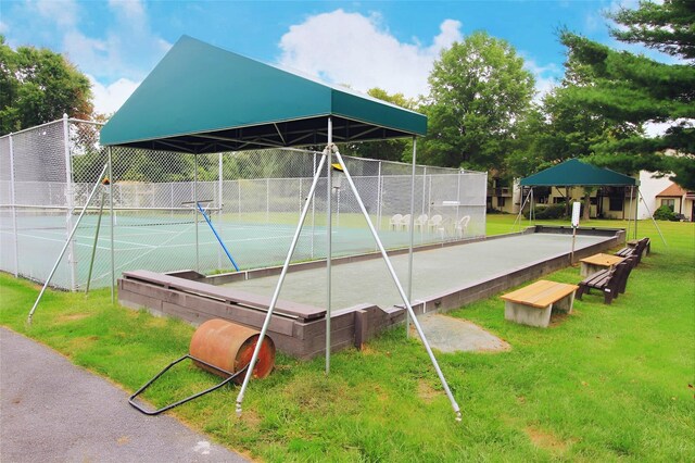 view of community with a yard, a tennis court, and fence