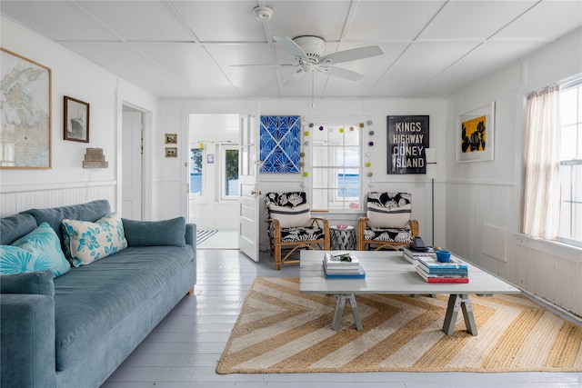 living area with a wainscoted wall, ceiling fan, and a wealth of natural light