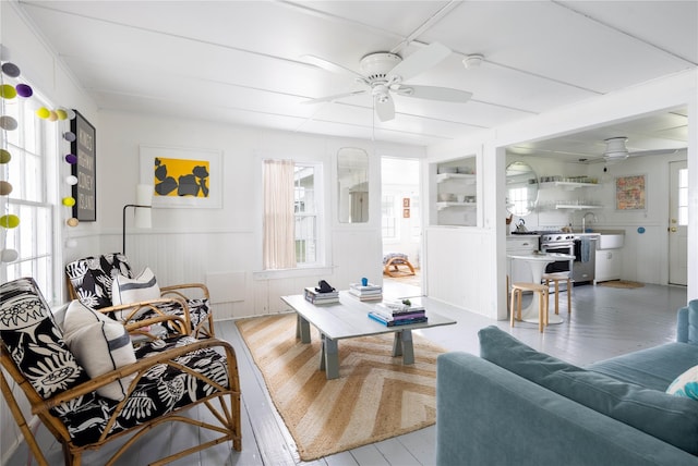 living area with light wood-style floors, plenty of natural light, a ceiling fan, and a wainscoted wall