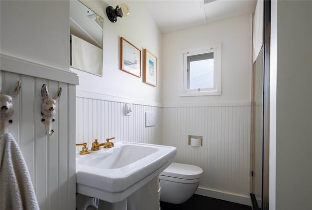 bathroom with toilet, a wainscoted wall, and a sink