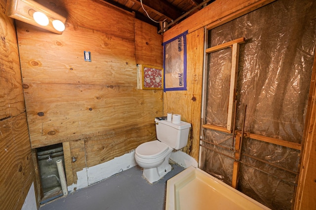 bathroom with toilet, wood walls, and finished concrete floors