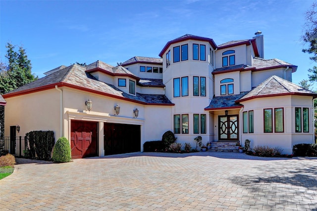 view of front of home with fence, an attached garage, stucco siding, a chimney, and decorative driveway