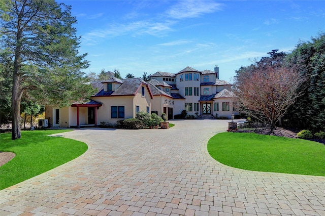 view of front of property with curved driveway, a chimney, a front yard, and stucco siding