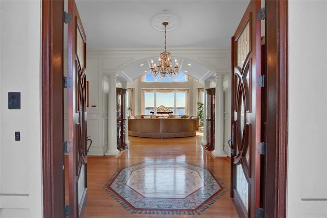 foyer featuring an inviting chandelier, arched walkways, decorative columns, light wood-type flooring, and ornamental molding