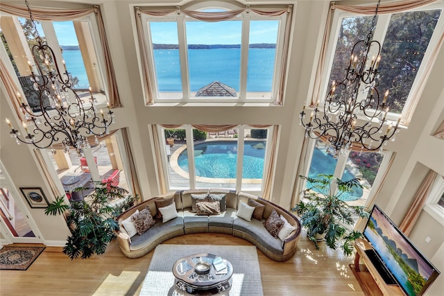living area featuring an inviting chandelier, a towering ceiling, wood finished floors, baseboards, and a water view