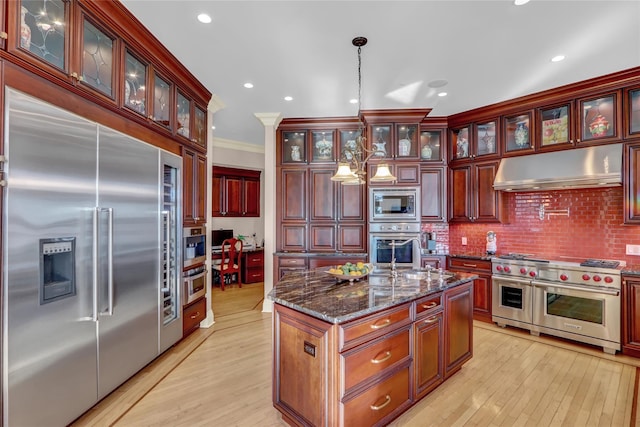 kitchen featuring built in appliances, light wood-style floors, reddish brown cabinets, under cabinet range hood, and hanging light fixtures