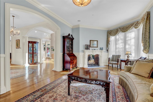 living room with crown molding, ornate columns, a warm lit fireplace, and wood finished floors