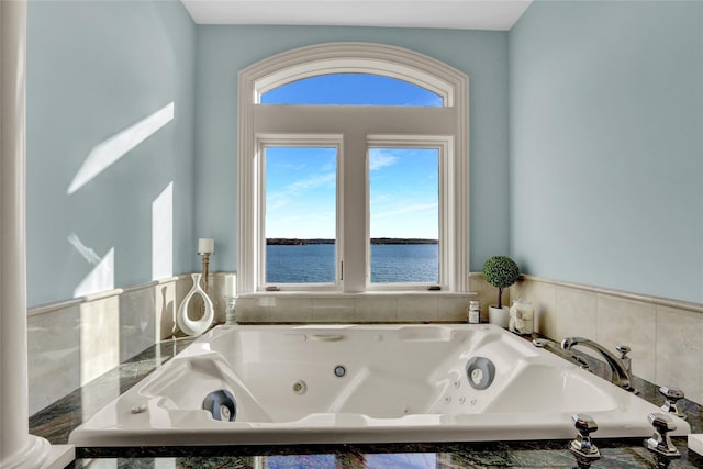 bathroom featuring a water view, a tub with jets, and a wealth of natural light