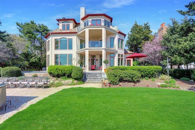 rear view of house featuring a lawn, stucco siding, a balcony, and a porch