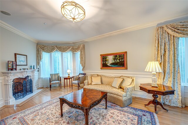 living room with ornamental molding, a fireplace with raised hearth, wainscoting, and wood finished floors