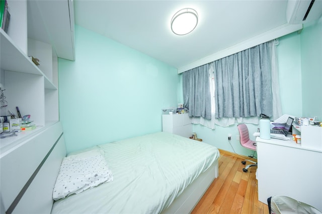 bedroom with an AC wall unit, light wood finished floors, and an office area