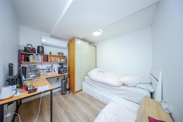 bedroom with a wall mounted air conditioner, light wood-style floors, and a desk