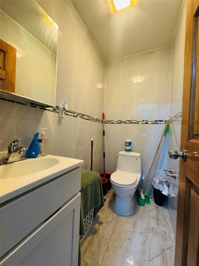 bathroom with tile walls, marble look tile flooring, toilet, and vanity