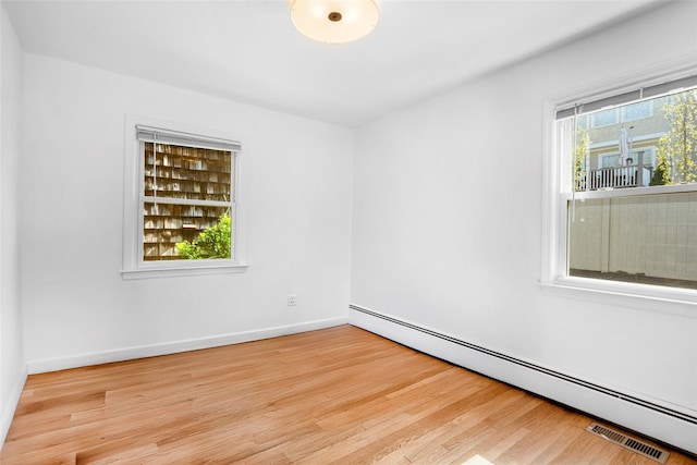 spare room featuring wood finished floors, baseboards, visible vents, and a baseboard heating unit
