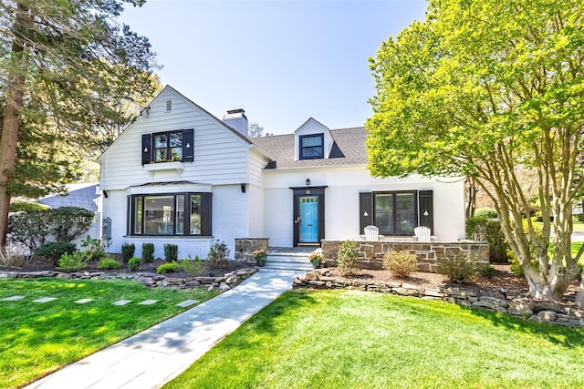 view of front of house featuring a front yard, a chimney, covered porch, and brick siding
